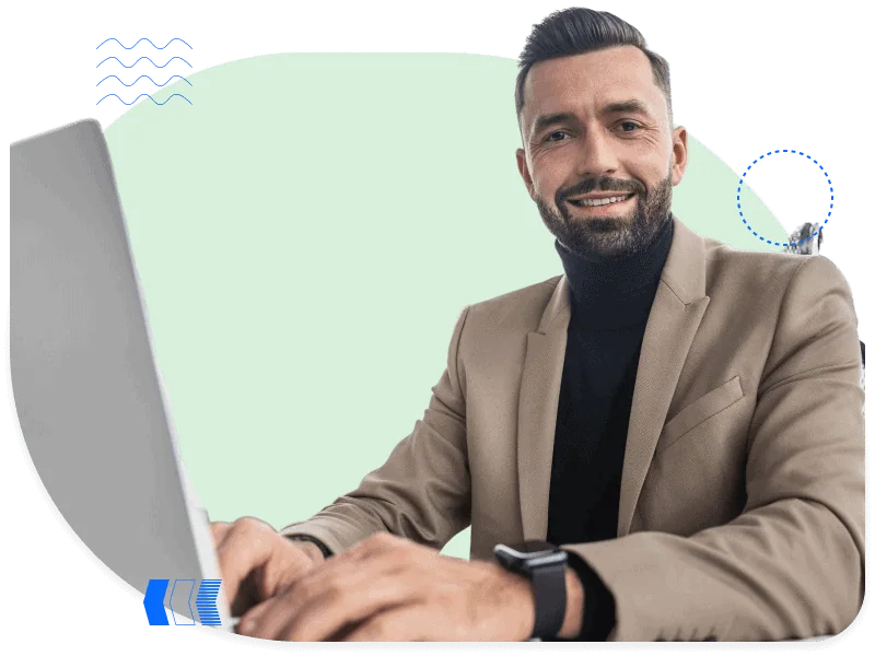 Confident businessman in beige blazer smiling at desk while working on a laptop, representing C-level decision makers
